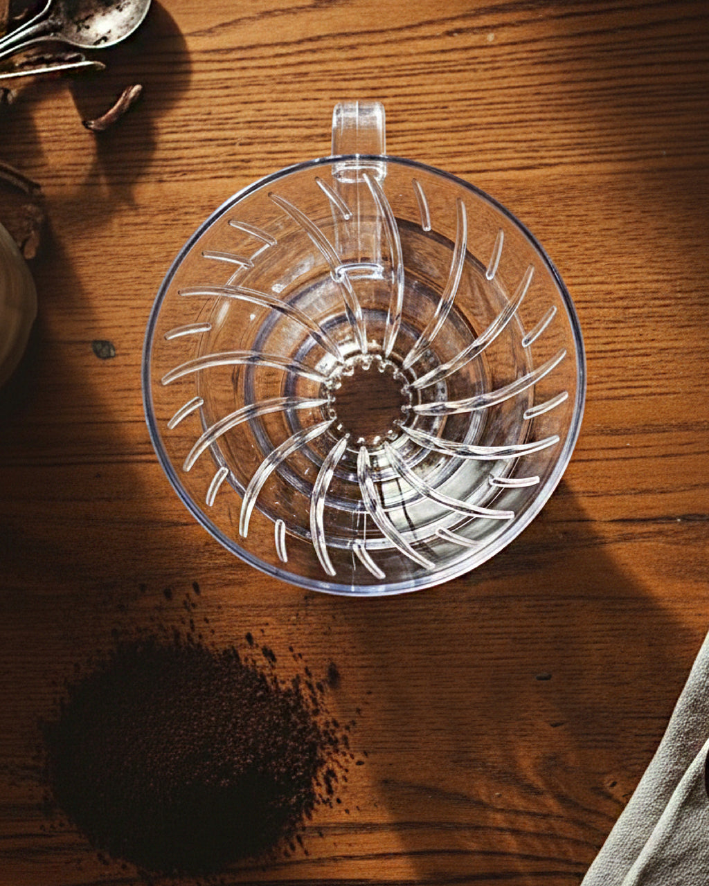 Vista cenital de un dripper V60 de acrílico sobre mesa de madera con café molido. Se aprecian las estrías internas en espiral para una extracción uniforme del café.