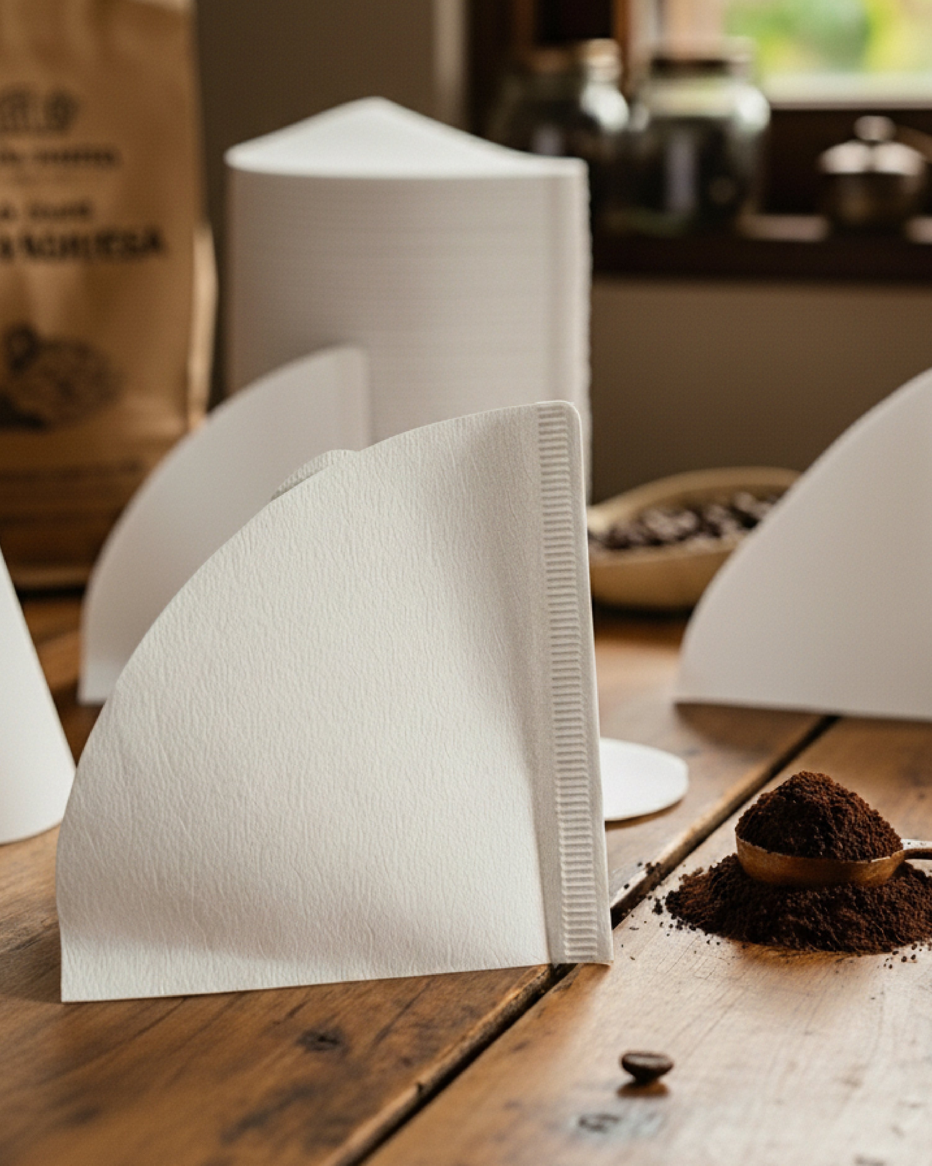 Filtro de papel blanco para café V60 en primer plano sobre mesa de madera rústica con una montaña de café recién molido. Accesorio esencial para el ritual de filtrado de Alma de Mariposa.