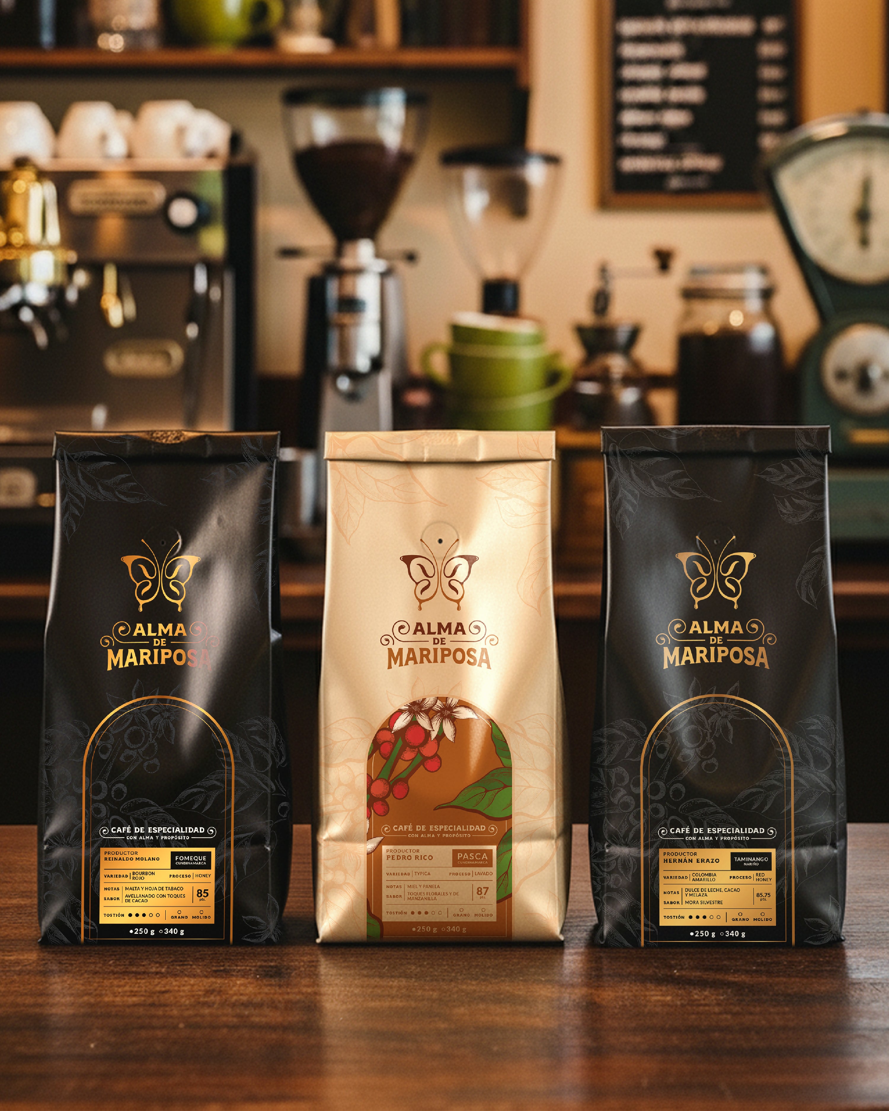 Tres bolsas de café de especialidad Alma de Mariposa de 250g sobre una barra de madera. Kit Trilogía de Orígenes con molino y máquina de espresso de fondo.