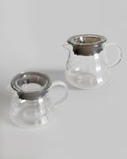 Dos jarras servidoras de vidrio transparente de 360 ml con tapa hermética sobre fondo gris claro. Diseño ergonómico y resistente para café filtrado en Alma de Mariposa.