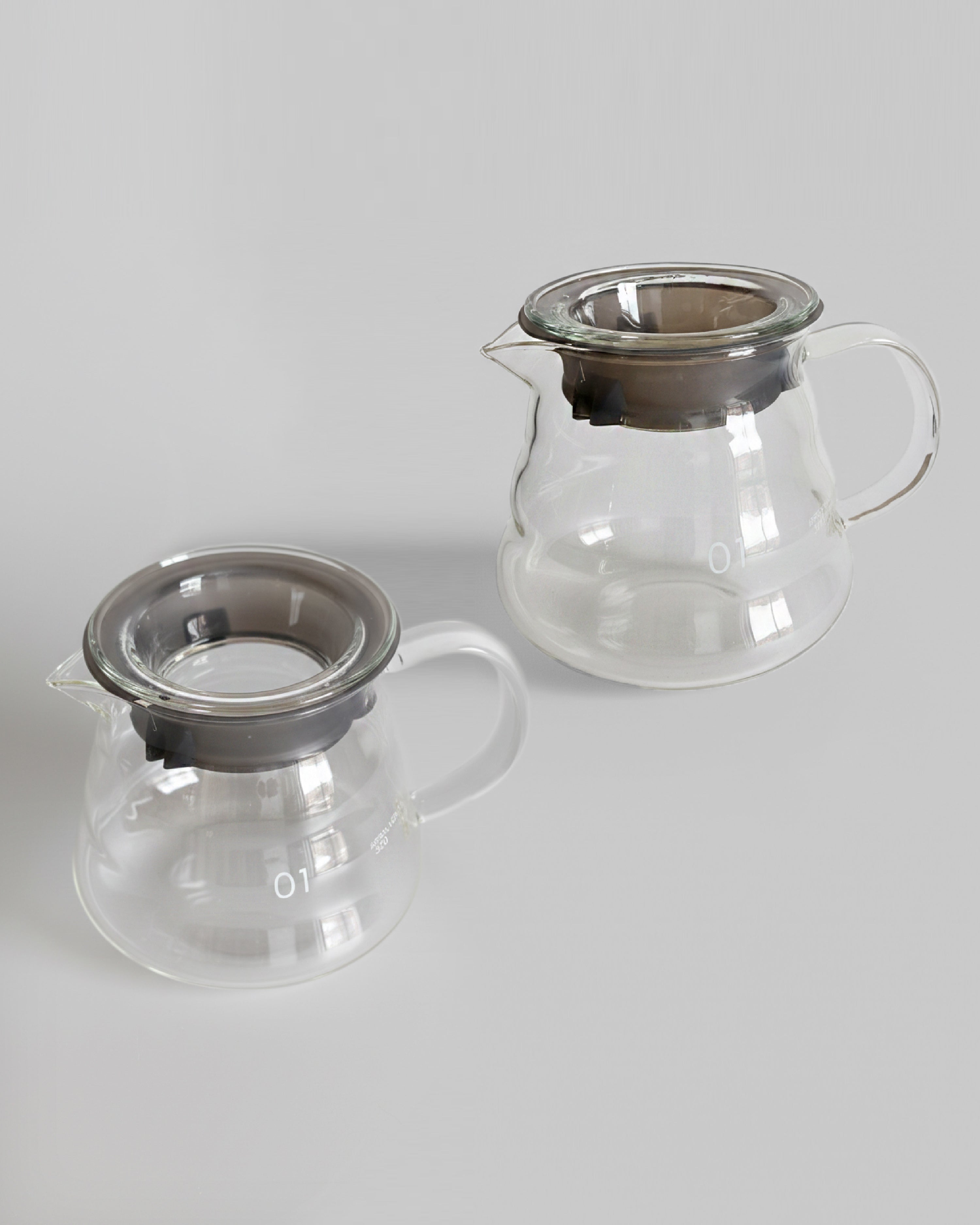 Dos jarras servidoras de vidrio transparente de 360 ml con tapa hermética sobre fondo gris claro. Diseño ergonómico y resistente para café filtrado en Alma de Mariposa.